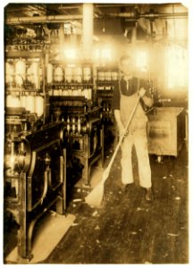 Boy holding broom near textile machinery LOC nclc.03057