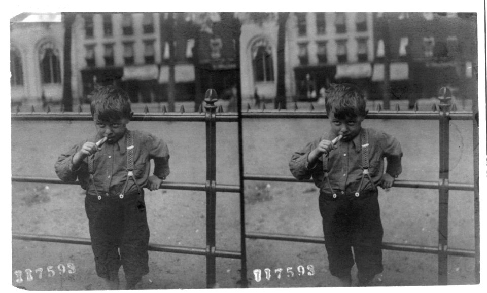 Boy standing along a railing and eating a peppermint stick LCCN2003656078