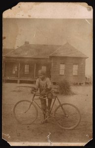 Boy standing next to a bicycle, house in the background LCCN2015652133