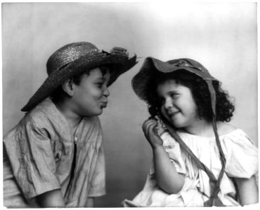 Boy wearing broken straw hat, with lips puckered, facing girl wearing bonnet LCCN96506058