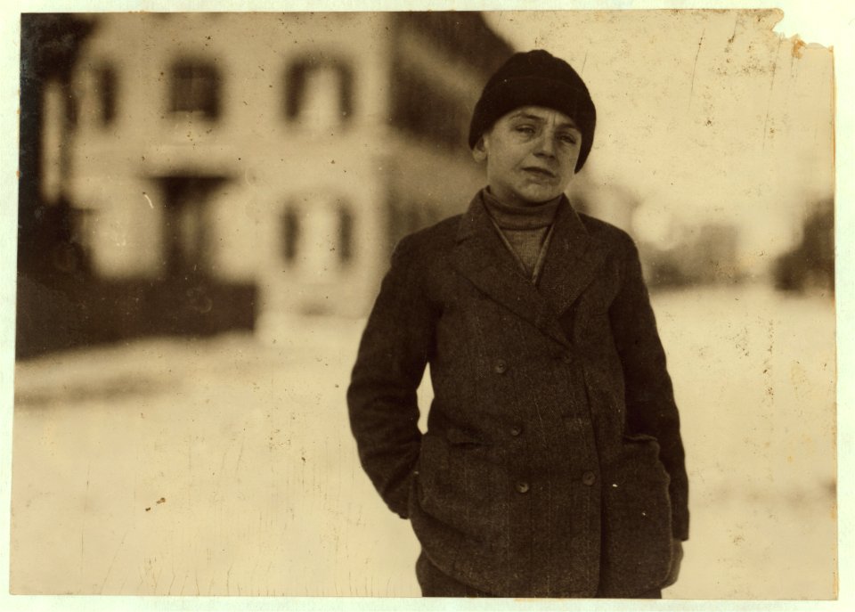 Boy wearing jacket and cap, with hand in his pocket, standing outdoors LOC nclc.02530