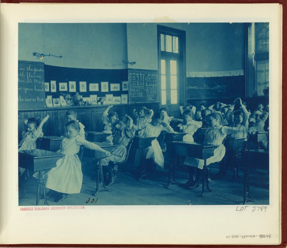 Children doing calisthenics while sitting at their desks in a classroom, 5th Division public schools, Washington, D.C. LCCN2008678867