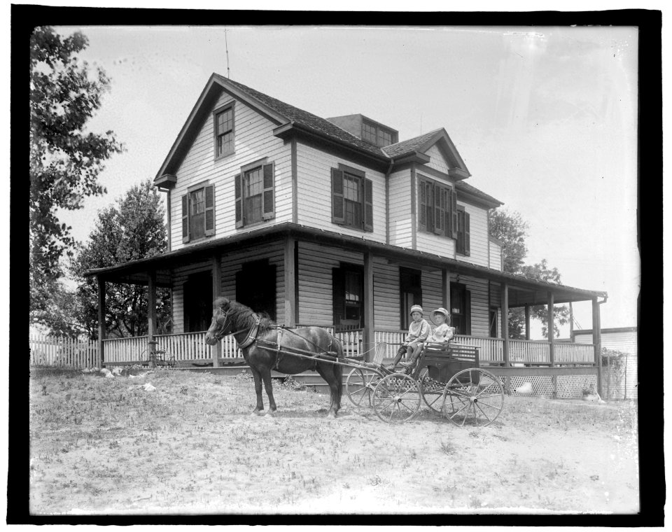 Children in horse-drawn wagon in front of house LCCN2016824377