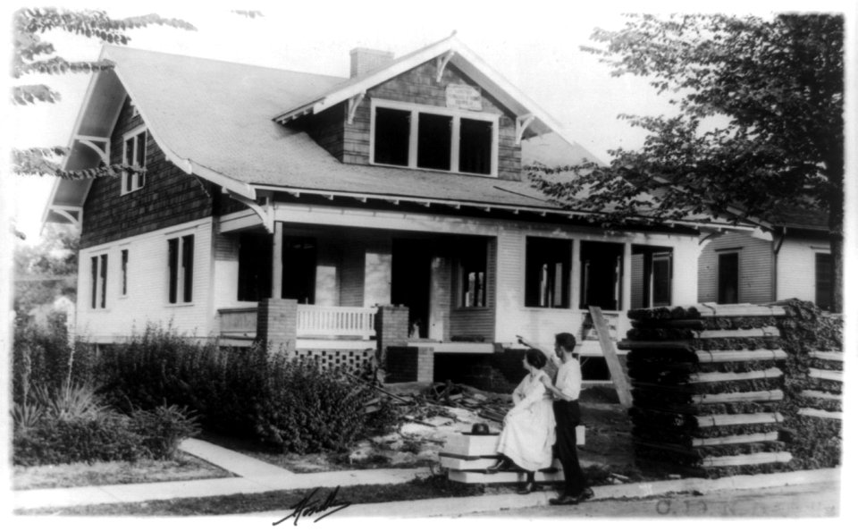 Couple looking at unfinished house, with wall laths out front LCCN89709284