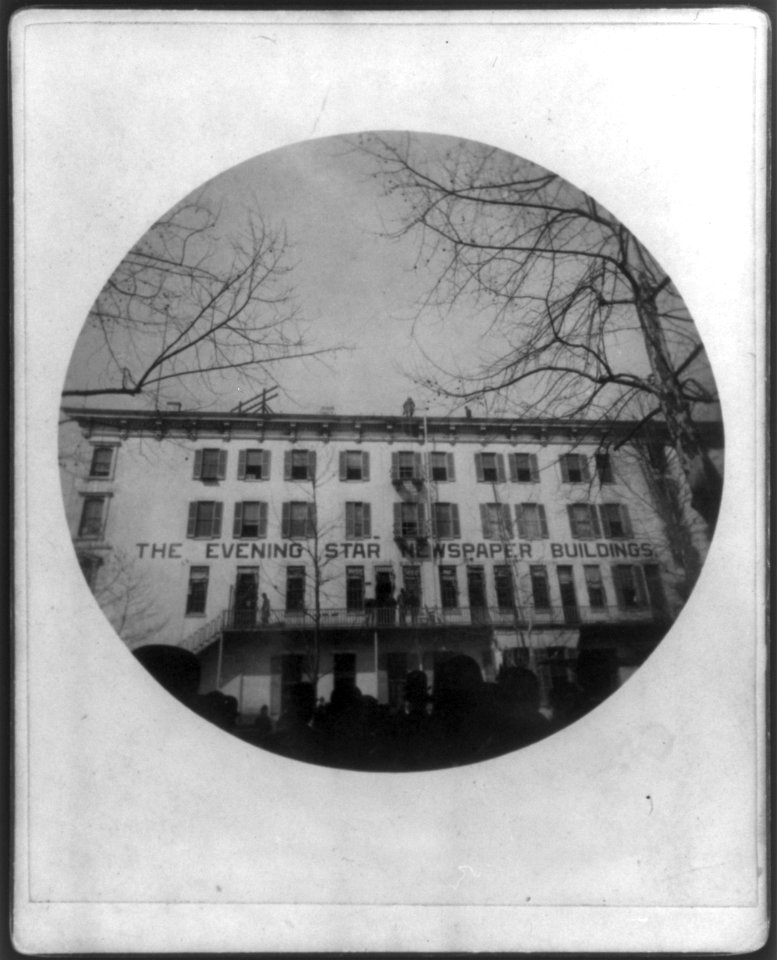 Crowd in front of the Evening Star Newspaper Buildings watching 2 men on roof, Washington, D.C. LCCN2005694602