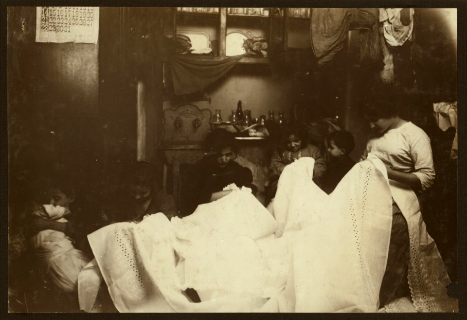 Cutting out embroidery on the dirty kitchen floor. Battista family, 259 E. 151 St. N.Y. On the right is the married daughter, who lives down stairs and usually works there. On her right next LOC nclc.04128