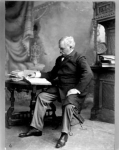 David B. Henderson, full-length portrait, seated at table reading a book LCCN2011645240