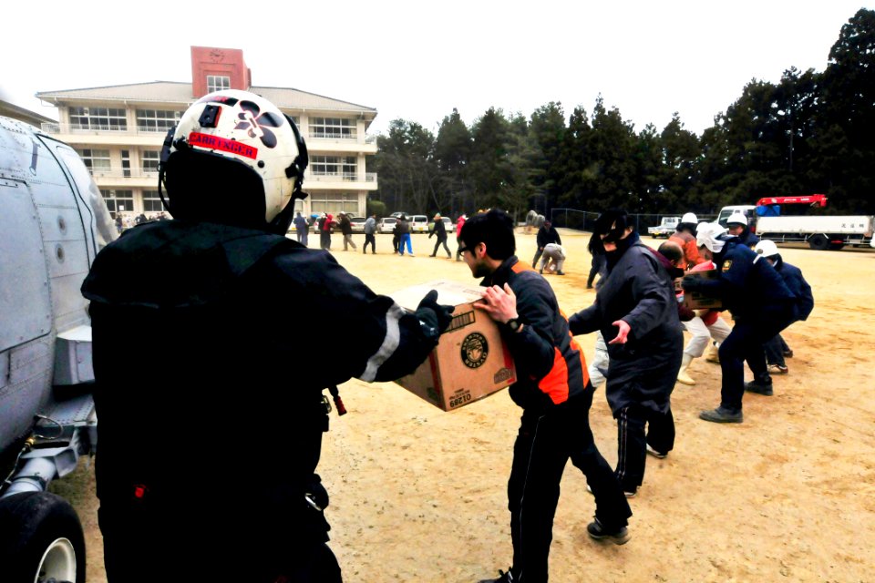 Defense.gov News Photo 110315-N-5503T-474 - U.S. Navy Petty Officer 2nd Class Chris Carringer passes a case of fresh water from an HH-60H Sea Hawk helicopter to a Japanese citizen during