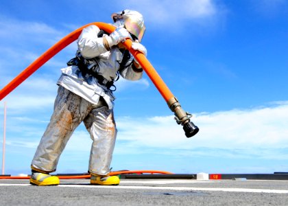 Defense.gov News Photo 110927-N-WJ771-108 - U.S. Navy Petty Officer 2nd Class Joshua B. Cary carries a charged fire hose across the flight deck of the amphibious transport dock ship USS Denver