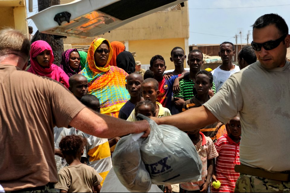 Djiboutian residents look on as U.S. Service members assigned to Camp Lemonnier, Djibouti, pass donated supplies into the home of a community leader in Djibouti city April 9, 2014 140409-N-LE393-091