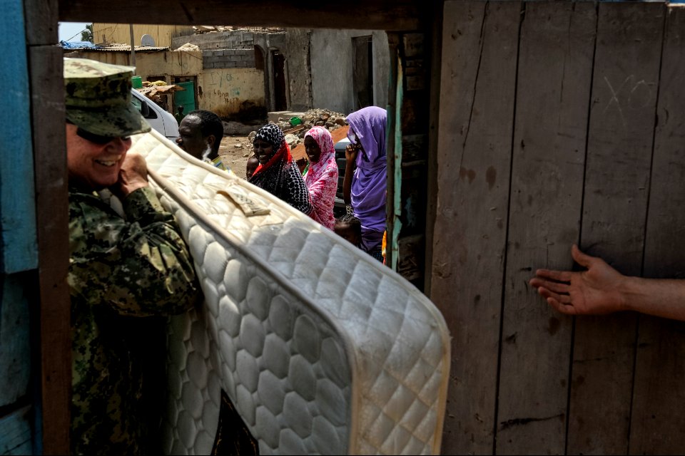 Djiboutian residents look on as U.S. Navy Cmdr. John Gayton, left, the command chaplain at Camp Lemonnier, Djibouti, carries a mattress into the home of a community leader in Djibouti city April 9, 2014 140409-N-LE393-054