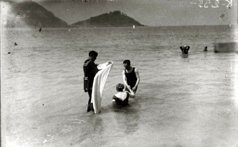 Bañero llevando la toalla a una bañista que sale del agua en la playa de la Concha (2 de 2) - Fondo Car-Kutxa Fototeka