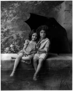 2 children on fountain wall, under umbrella in rain LCCN2003675183