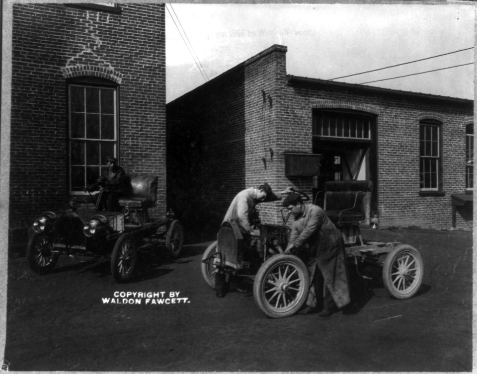 2 men working on an automobile outside of automobile plant LCCN2002707037