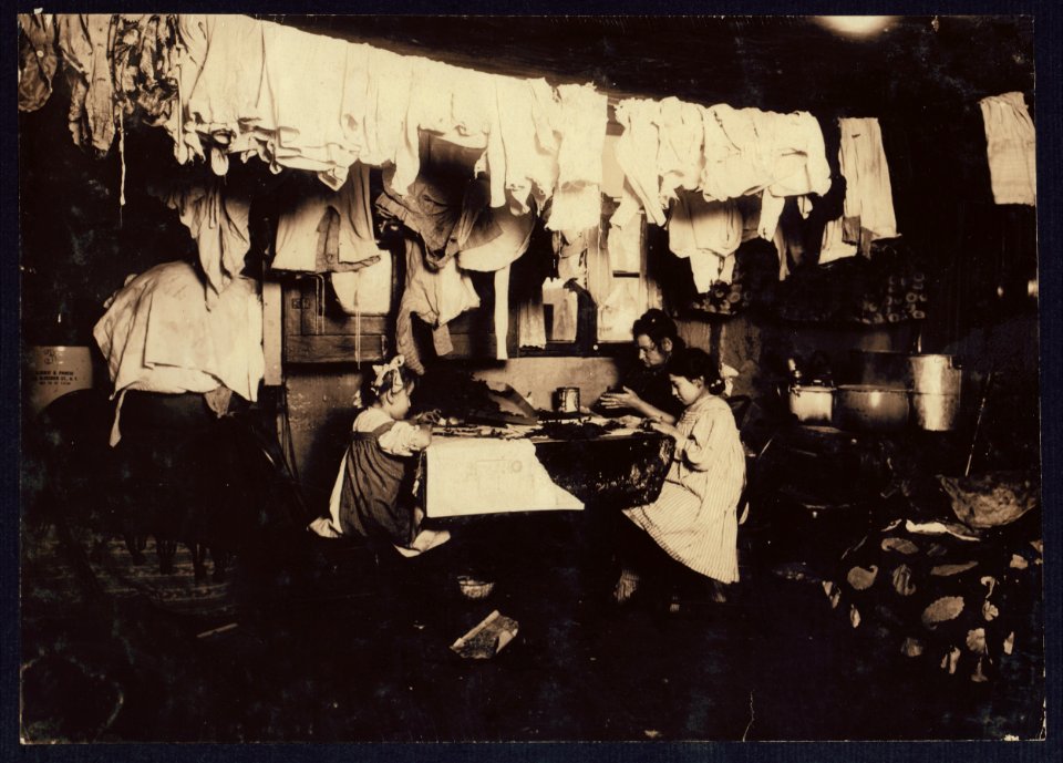 4 P.M. Ceru family, 143 Thompson St., near tenement, N.Y. In this dirty attic home with a dog and a cat adding to the other filth that accumulates, these three make artificial leaves. The LOC cph.3b01104