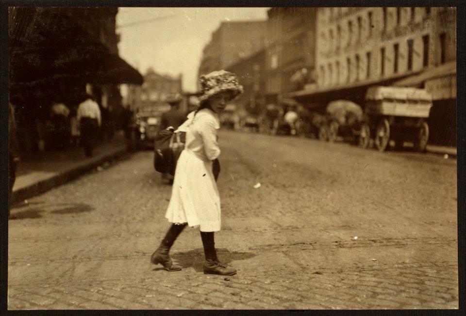 9 year old girl carrying garments down Blackstone Street, Boston, Mass., to a Hanover Street home. She finishes 8 pairs of trousers a day and gets 8 cents a piece. LOC nclc.04229