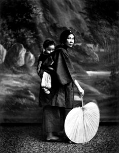 A Chinese woman with her child on her back and a fan in her hand photo