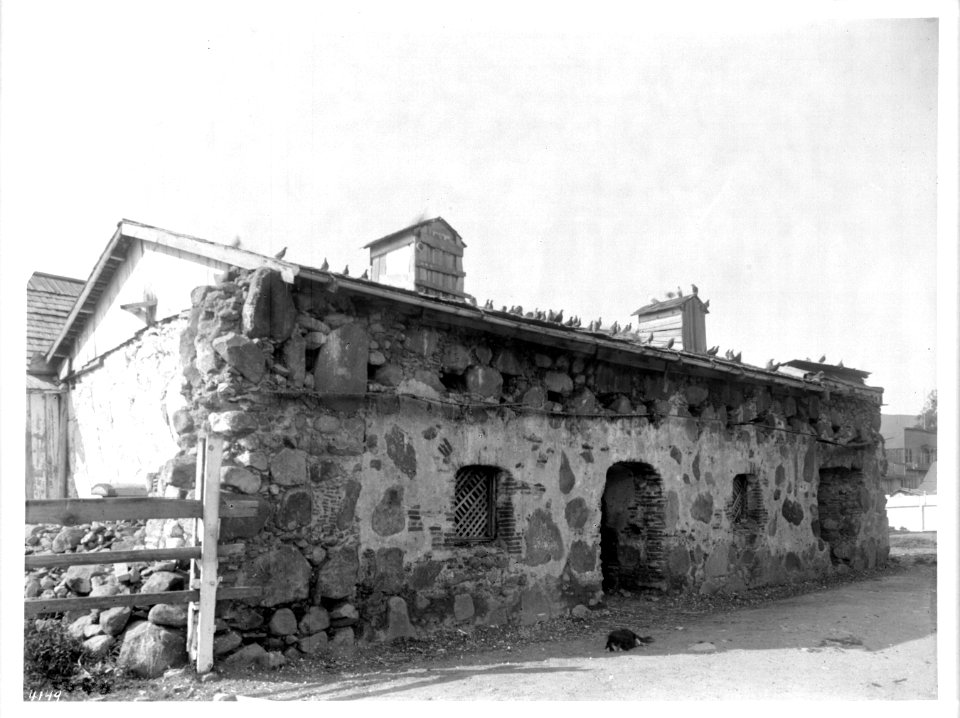 A dog sleeps on the ground in front of the Priests' residence of Mission San Luis Obispo de Tolosa, ca.1900 (CHS-4149)