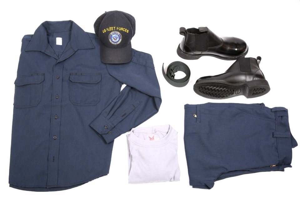 A display of the dark blue over dark blue two-piece flame-resistant organizational clothing variant prototype intended for E6 and below sailors along with the molder boot, rigger’s belt, undershirt and ball cap as compone