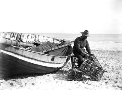 A fisherman in sou'wester mending lobster-crab creels on the beach alongside a beached Sheringham crab boat. RMG P27501 photo