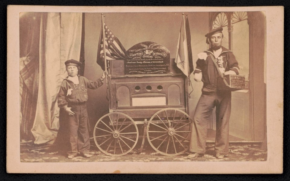 Bernard Tobey, a double amputee and his son, wearing Union sailor uniforms, standing beside a small wagon displaying Secretary of War Edwin Stanton's dispatch on the fall of Fort Fisher) - LCCN2017659614