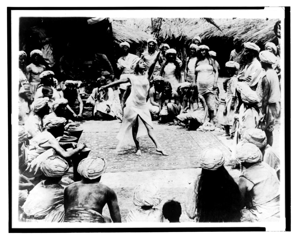 Between savage and tiger. Nautch girl dancing on rug with Hindoo men and women watching LCCN2003675560
