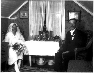 Brud och brudgum som sitter på var sin sida om ett bord med bröllopspresenter - Nordiska Museet - NMA.0035410 photo