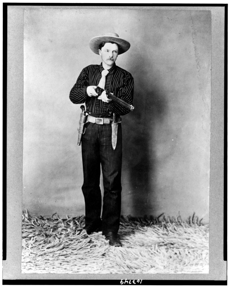 Bill Bennett, full-length portrait, standing, facing slightly right, holding rifle LCCN91787981