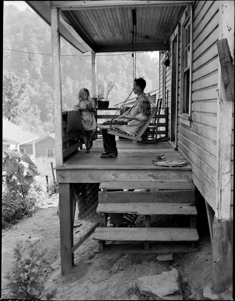 Bill Daniels, a miner, and his two daughters on the front porch of their three room house for which they pay $7... - NARA - 540998