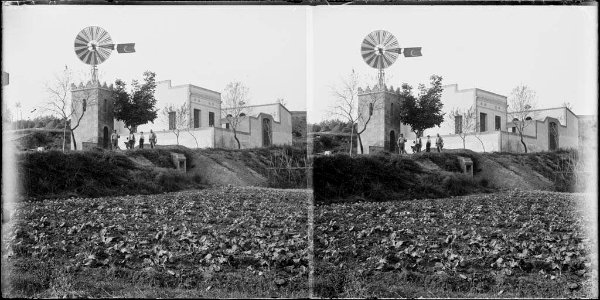 Camps de conreu amb un grup d'homes al costat d'una torre amb un molí de vent i alguns edificis