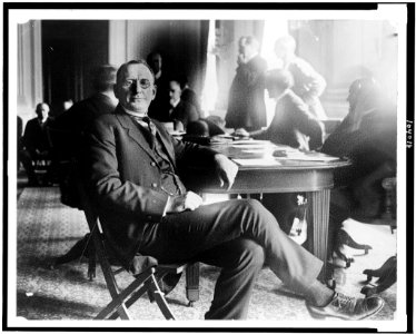 Col. William Joseph Simmons, full-length portrait, seated at table during House committee investigation of the Ku Klux Klan; men standing and seated in background LCCN91792441