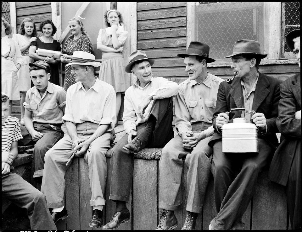 Blaine Sergent, with pulled-up leg, talks with his miner friends on the front porch of the company store on a... - NARA - 541331