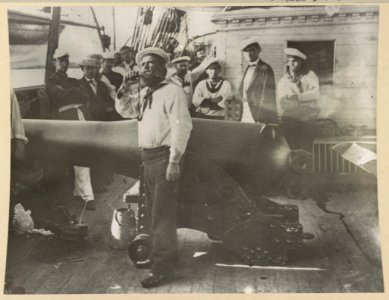 Boatswain piping in front of large cannon on deck of U.S. Naval warship; other sailors standing in background LCCN2013647460