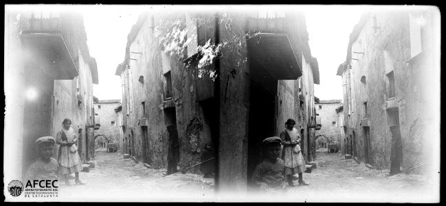Carrer de Vilanova de l'Aguda amb un nen, una noia i u home en un portal