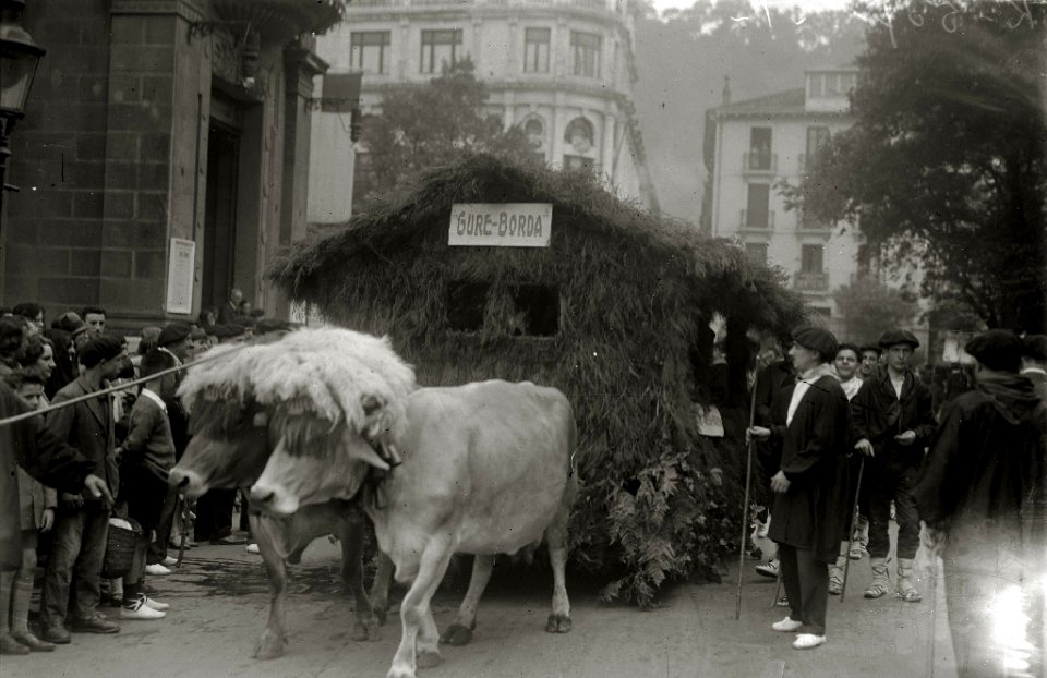 Carroza tirada por bueyes representando una borda con una comparsa de personas vestidas de caseros, desfilando por una calle de San Sebastián durante unas 'Fiestas Euskaras' (2 de 2) - Fondo Car-Kutxa Fototeka