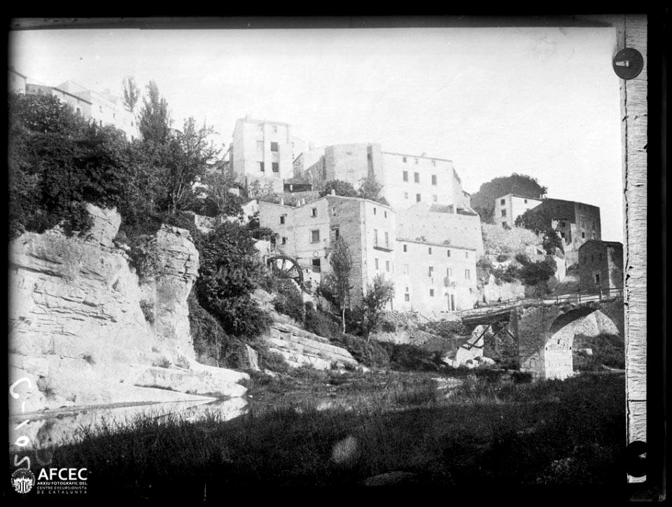 Cases de la Riba des de la part baixa del poble amb el riu i un pont en primer terme