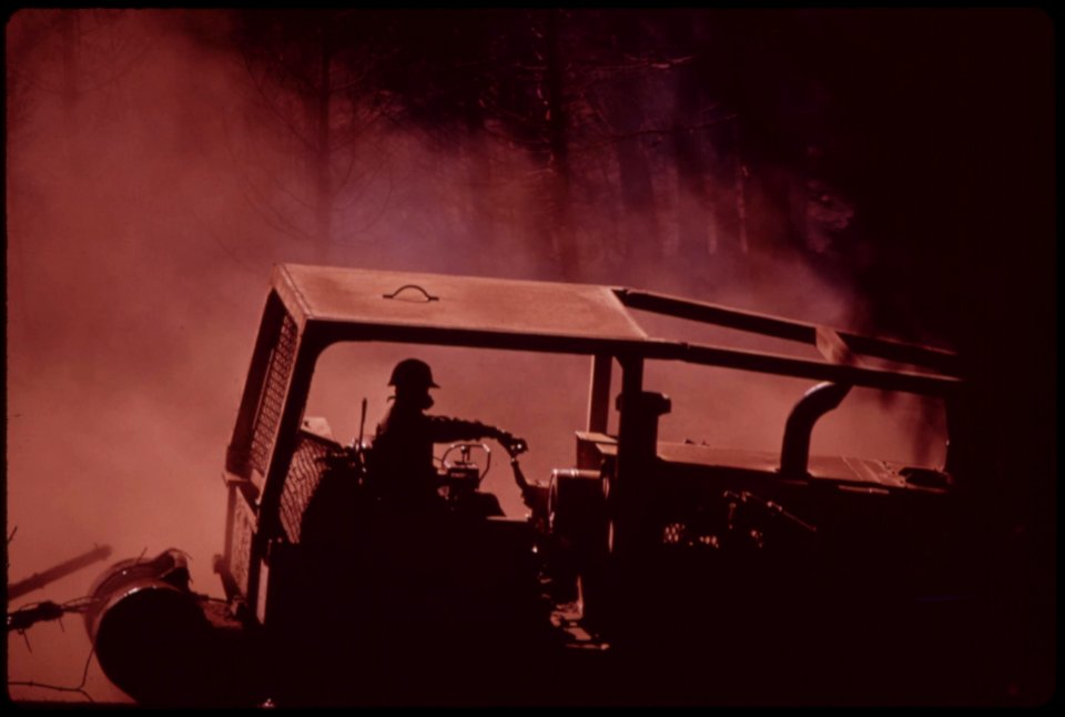 Caterpillars-work-in-dust-and-soot-hauling-logs-to-landing-area-where-they-will-be-loaded-onto-trucks-face-mask-filters-ash-and-soot-filled-air-so-driver-can-breathe-september-1973 7153114575 o
