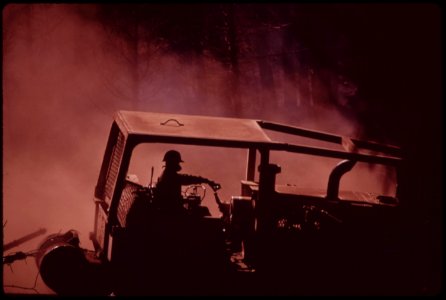 Caterpillars-work-in-dust-and-soot-hauling-logs-to-landing-area-where-they-will-be-loaded-onto-trucks-face-mask-filters-ash-and-soot-filled-air-so-driver-can-breathe-september-1973 7153114575 o