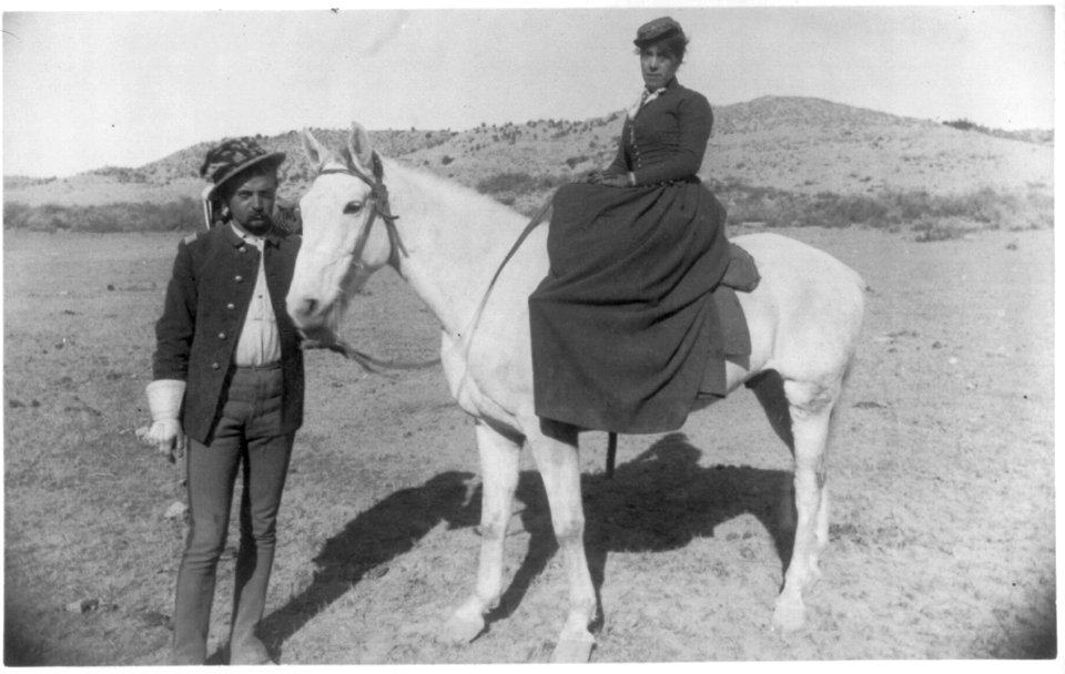 Cavalry officer holding white horse carrying woman; each is wearing the other's hat; Fort Verde, Ariz., 1884-87 LCCN2004679563
