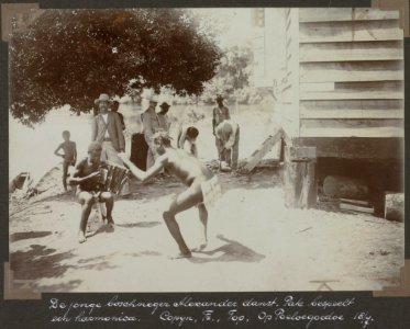 Collectie NMvWereldculturen, RV-A103-1-9, 'De jonge boschneger Alexander danst. Pale bespeelt een harmonica. Op Poeloegoedoe (18 Juli 1904)'. Foto- G.M. Versteeg, 18 juli 1904