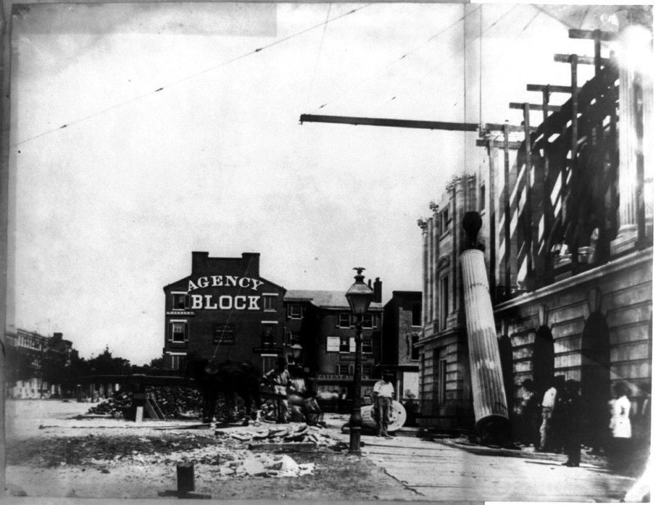Column being raised into position, U.S. Post Office, with building named Agency Block in background LCCN2002717755