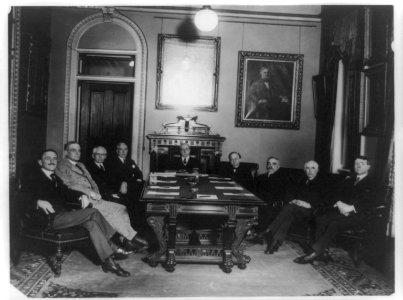 Charles Evans Hughes seated at head of table, with eight other men around the table in the Diplomatic Room of the State Department LCCN89709659