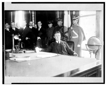 Charles Seymour Whitman, half-length portrait seated at desk, with dignitaries behind him, on the occassion of his inauguration as governor of New York state, Albany, 1915 LCCN2003668187