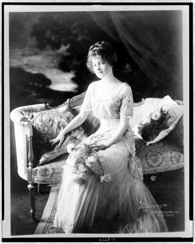 Dolorita O'Gorman, full-length portrait, seated, facing slightly left, holding flowers) - Marceau LCCN97506832