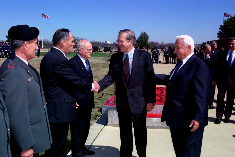 Donald Rumsfeld stands beside Ariel Sharon as he greets members of the Israeli delegation