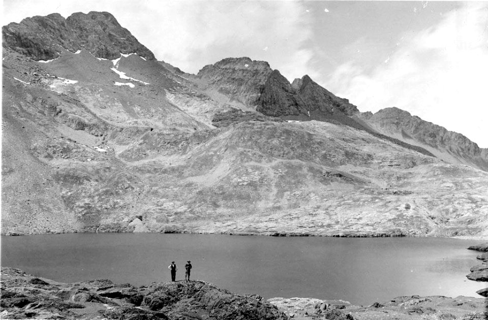 Dos homes a la riba de l'estany de Cregüeña i al fons muntanyes