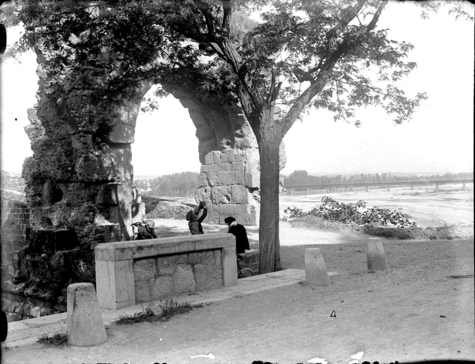Dos homes menjant a l'ombra d'un arbre junt a l'arc romà de Castellbisbal (AFCEC RIBASV C 2590)