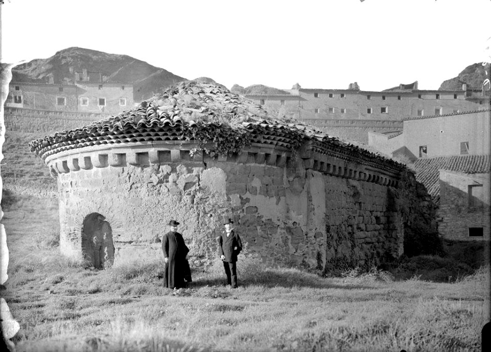 Dos homes, un d'ells sacerdot, al costat de la porta de l'absis de la capella de Sant Miquel