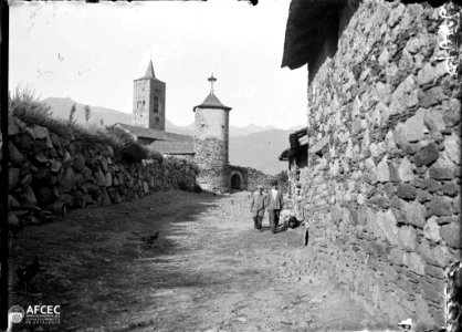Dos nens en un carrer i al fons l'església de Sant Just i Sant Pastor i torre de les hores del poble de Son