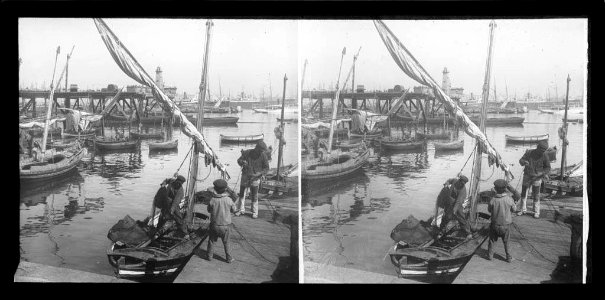 Dos pescadors i un nen carregant una xarxa a un llagut al port de Barcelona